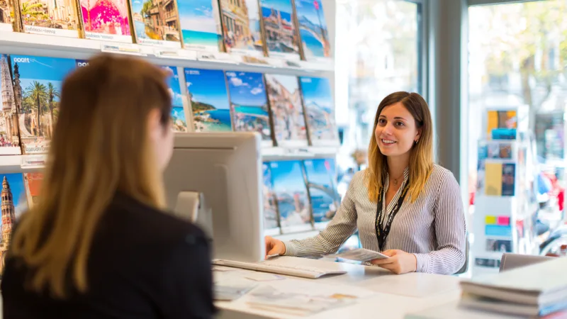 Il banco di un’agenzia viaggi: un biglietto stampato passa di mano a due visitatori
